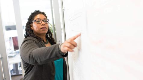 a black woman stands at a whiteboard giving a lesson