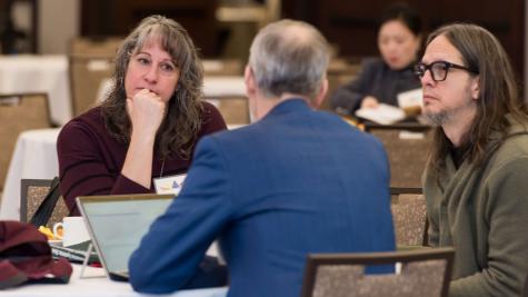 Three people have a conversation at a table.