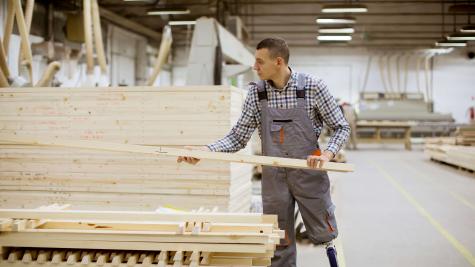 A person with a prosthetic leg lifts a piece of lumber from a pile. 