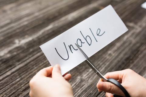 Someone cutting "un" from a card saying "unable" to make it say "able"