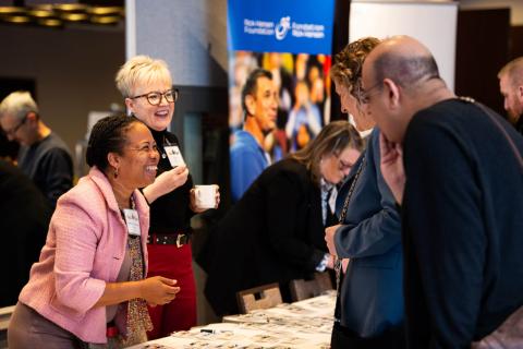 A group of people surround the welcome table. They smile, laugh, and talk with each other
