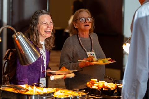 Two people hold full plates of food from the buffet. They smile at someone off camera