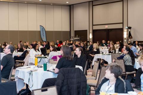 A crowd of people sitting at tables in a large conference room.