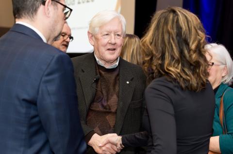 Two people shake hands and converse while another person watches on.