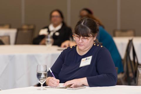A person sits at a table writing in a notebook.