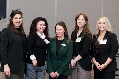 A group of five people huddle together and smile for a photo