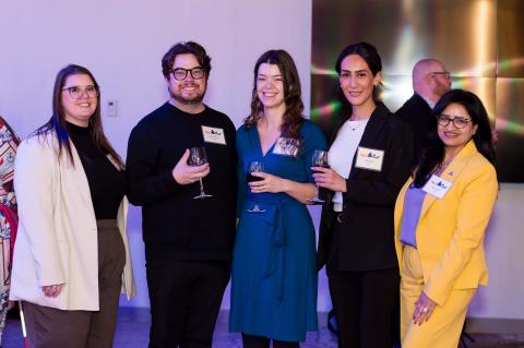 A group of five people pose and smile for a photo with wine glasses in their hands