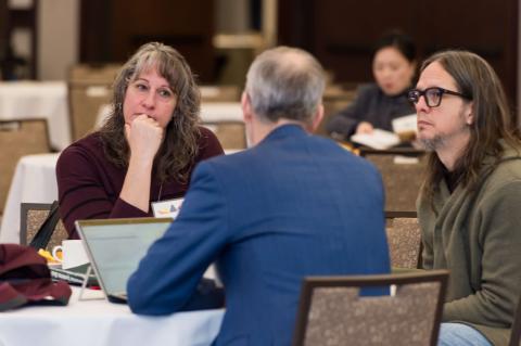 Three people have a conversation at a table.