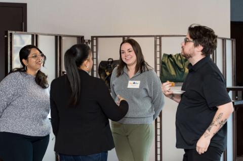 Four people stand in a group facing each other. They talk and smile.