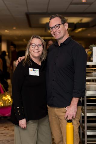 Two people pose for a picture together. They smile at the camera.