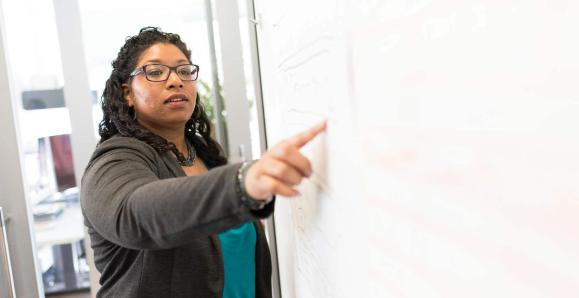 a black woman stands at a whiteboard giving a lesson