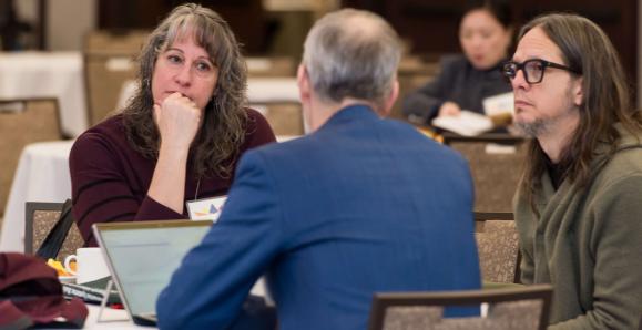 Three people have a conversation at a table.