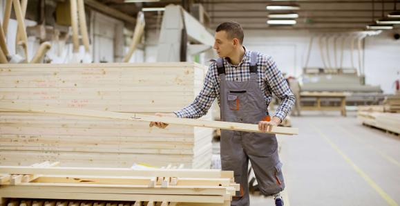 A person with a prosthetic leg lifts a piece of lumber from a pile. 