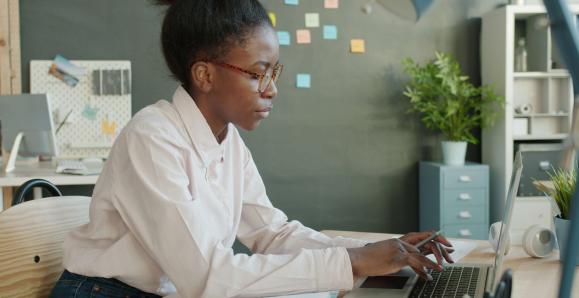 A person sitting at their laptop in front of a wall of sticky notes.