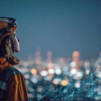 A young woman wearing a hardhat, looking out over a city at night
