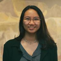 Professional headshot of Janice Lam wearing glasses and a dark blazer, smiling in front of a neutral background.