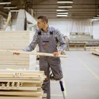 A person with a prosthetic leg lifts a piece of lumber from a pile. 