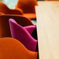 A series of chairs at a table. Orange chairs surround one singular pink chair.