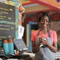 A worker wearing an apron and writing on a notepad standing behind the counter of a cafe. 