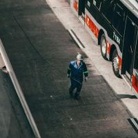 A person walking on a sidewalk beside a parked bus.