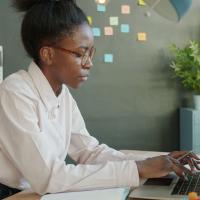 A person sitting at their laptop in front of a wall of sticky notes.
