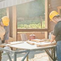 Two construction workers working at a saw bench. They are wearing hard hats.